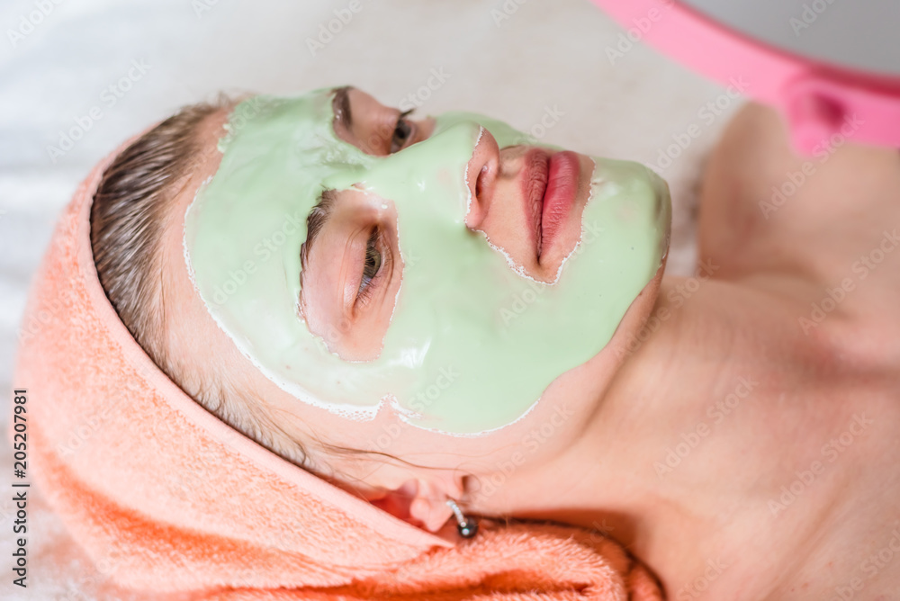 Fototapeta premium Young woman lying with a towel on his head and cosmetic algae mask on her face - beauty treatment close-up