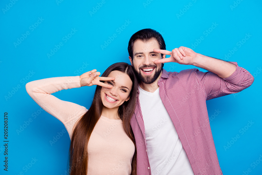 Portrait of funky trendy couple gesturing v-sings near face, celebrating valentine day, looking at camera isolated on blue background Portrait of funky trendy couple gesturing v-sings near face, celebrating valentine day, looking at camera isolated on blue background