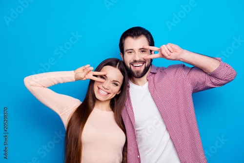 Portrait of funky trendy couple gesturing v-sings near face, celebrating valentine day, looking at camera isolated on blue background