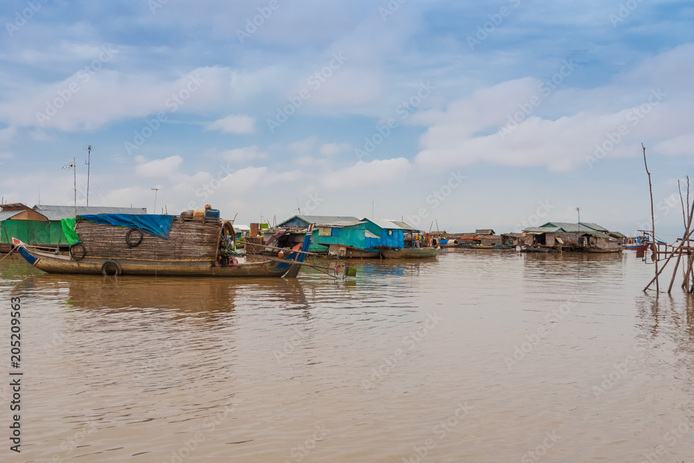 View of the floating houses in Cambodia's floating village Chong Kneas on Tonle Sap Lake. On the left is a wooden sampan-like boat including a small shelter with a curved roof anchored.