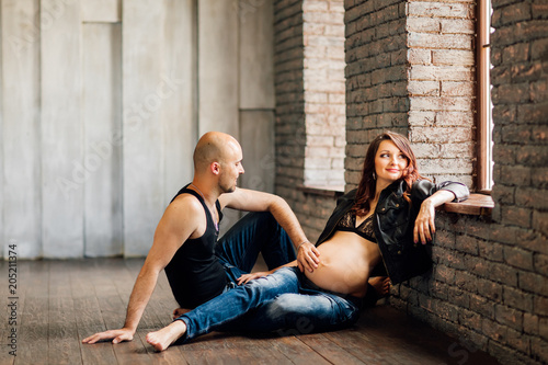 Young pregnant woman with her husband sitting on the floor near the window in the studio