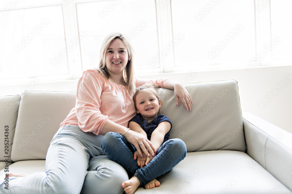 Portrait of beautiful mother and her little daughter sitting together on couch Portrait of beautiful mother and her little daughter sitting together on couch