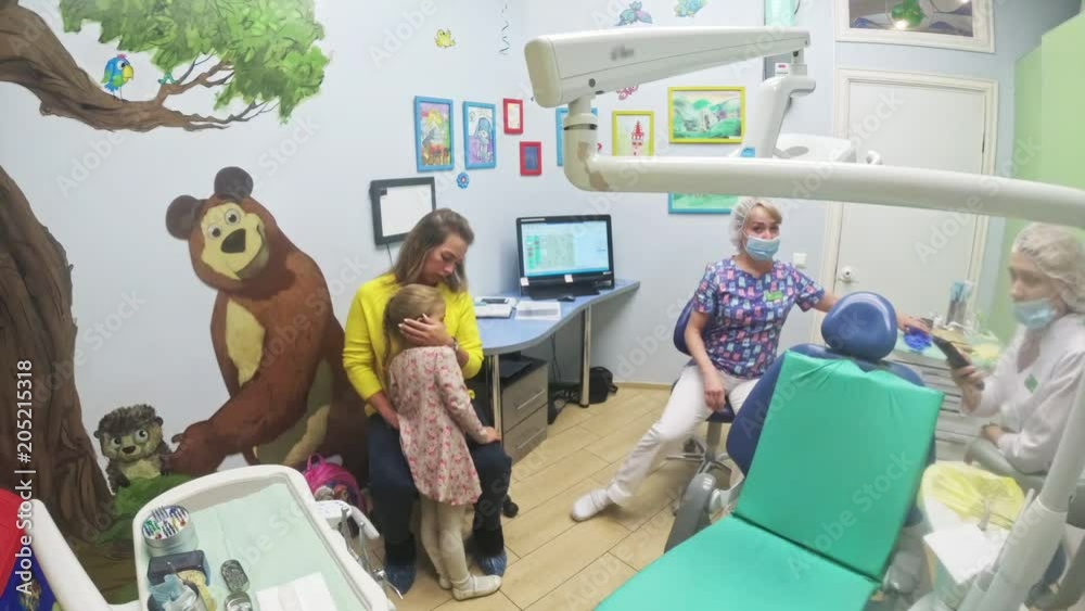 Child with a mother at a dentist's reception. The girl lies in the chair, behind her mother. The doctor works with an assistant. Procedure for drilling a tooth. Setting a temporary seal. Using the x