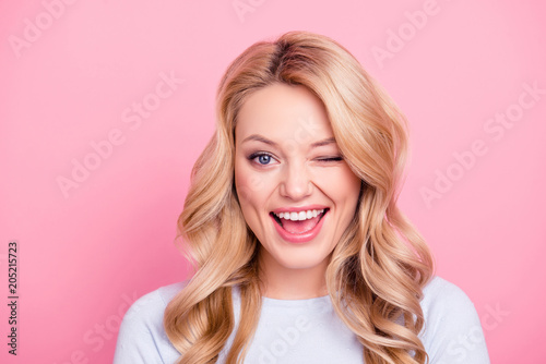 Portrait of funny foolish girl with modern hairdo winking with one eye open mouth, playing with lover isolated on pink background