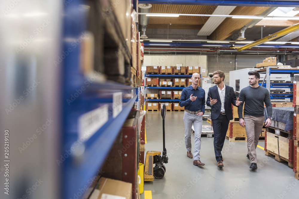 Three men walking and talking in factory storeroom Three men walking and talking in factory storeroom