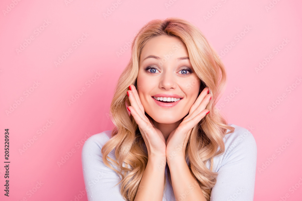 Obraz premium Portrait of cute naive big eyed woman with modern hairdo holding palms near cheeks looking at camera isolated on pink background