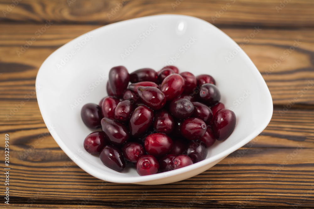Full white ceramic bowl of red fresh raw dogwood berry on old wooden rustic table Full white ceramic bowl of red fresh raw dogwood berry on old wooden rustic table