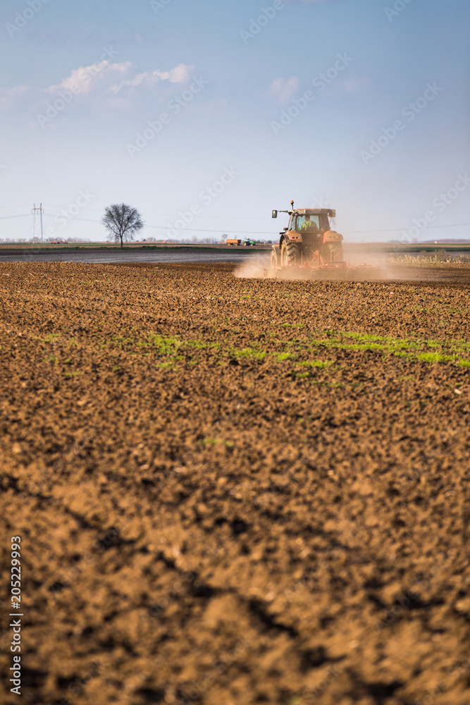 Fototapeta premium Farmer in tractor preparing land with seedbed cultivator as part of pre seeding activities in early spring season of agricultural works at farmlands.