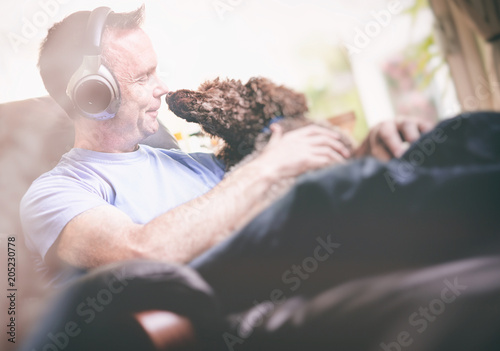 A man enjoying listening to music on wireless headphones in a relaxing armchair. Styling and grain effect added to image. photo