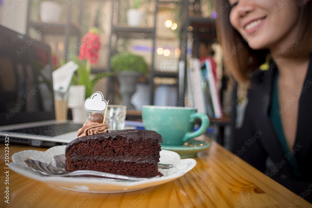 The chocolate cake is on the table in the coffee shop with businesswoman as the background.