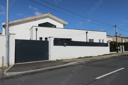 a recent white and gray house with a large protective wall and a dark gray automatic gate