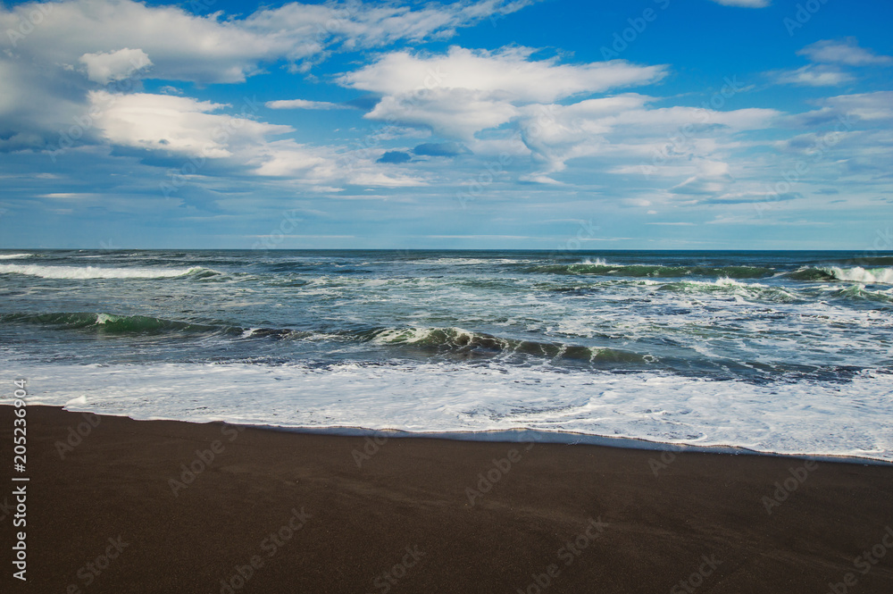Halaktyr beach. Kamchatka. Russian federation. Dark almost black color sand beach of Pacific ocean. Stone mountains and yellow grass are on a background. Light blue sky Halaktyr beach. Kamchatka. Russian federation. Dark almost black color sand beach of Pacific ocean. Stone mountains and yellow grass are on a background. Light blue sky