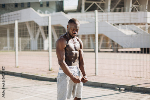 Seductive African American man with muscels poses with naked chest before the fence photo