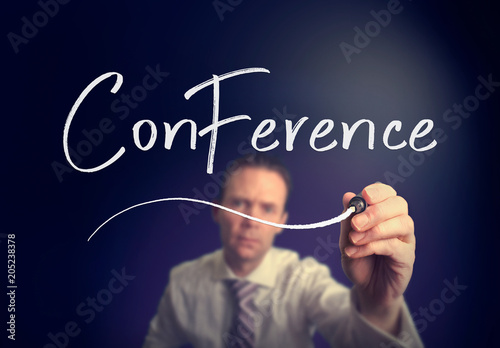 A businessman writing a Conference concept with a white pen on a clear screen.