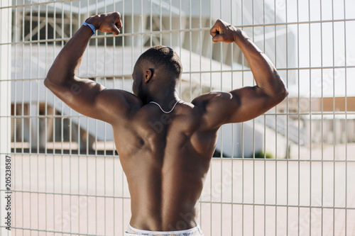 Seductive African American man with muscels poses with naked chest before the fence photo