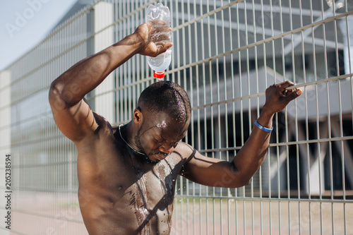 Seductive African American man with muscels poses with naked chest before the fence