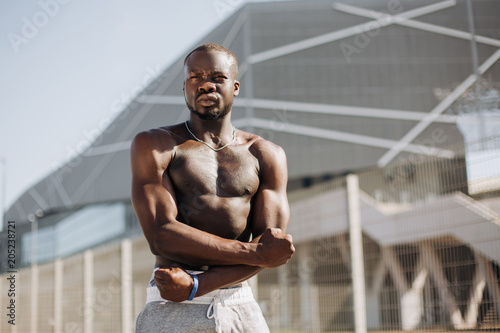 Seductive African American man with muscels poses with naked chest before the fence photo