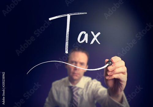 A businessman writing a Tax concept with a white pen on a clear screen.