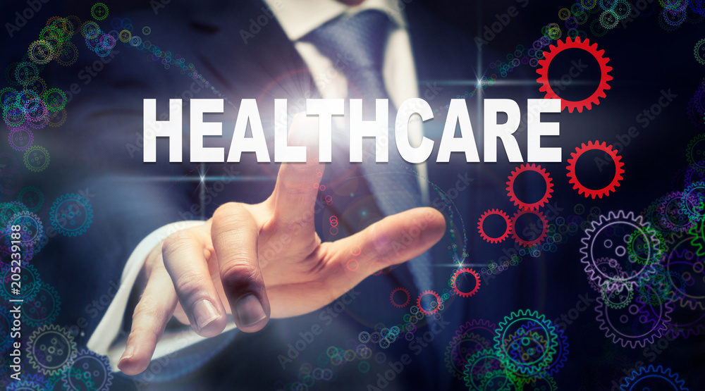 A businessman pressing a Healthcare business concept on a graphical display of cogs A businessman pressing a Healthcare business concept on a graphical display of cogs