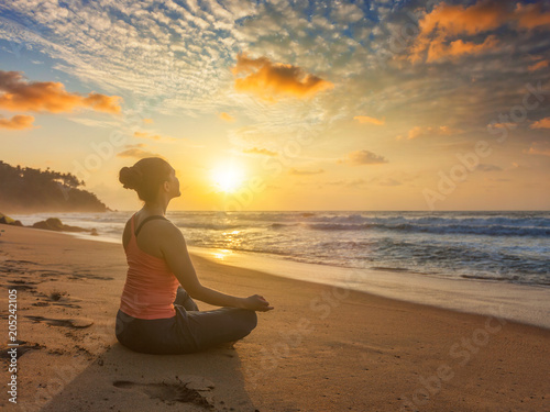 Woman doing yoga oudoors at beach - Padmasana lotus pose
