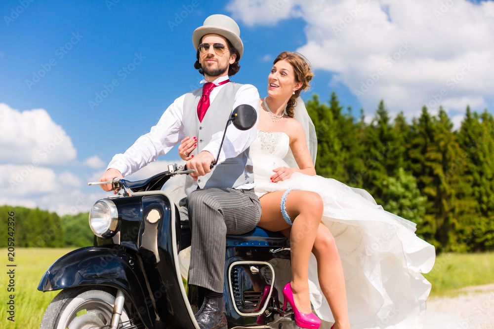 Wedding concept, bride and groom on motor scooter, she is showing her garter on leg Wedding concept, bride and groom on motor scooter, she is showing her garter on leg