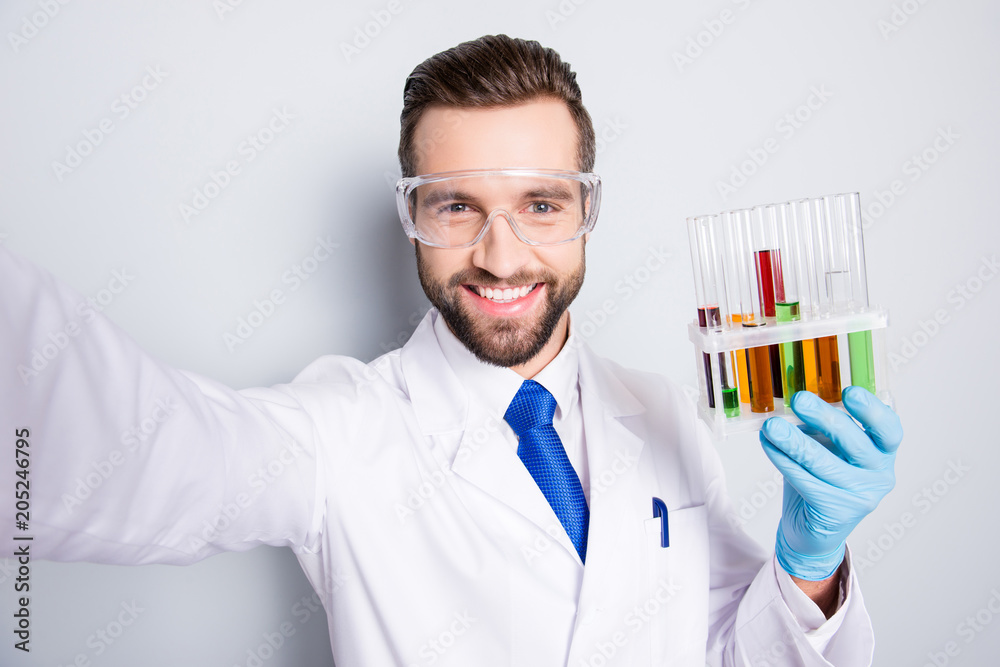 Self portrait of positive trendy scientist showing test tubes with multi-colored liquid, shooting selfie on front camera, having video-call, isolated on grey background Self portrait of positive trendy scientist showing test tubes with multi-colored liquid, shooting selfie on front camera, having video-call, isolated on grey background