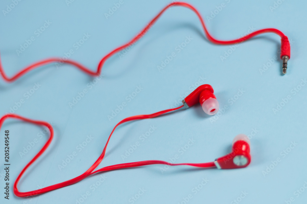 Red new earphone with cable and metal plug on blue paper background Red new earphone with cable and metal plug on blue paper background