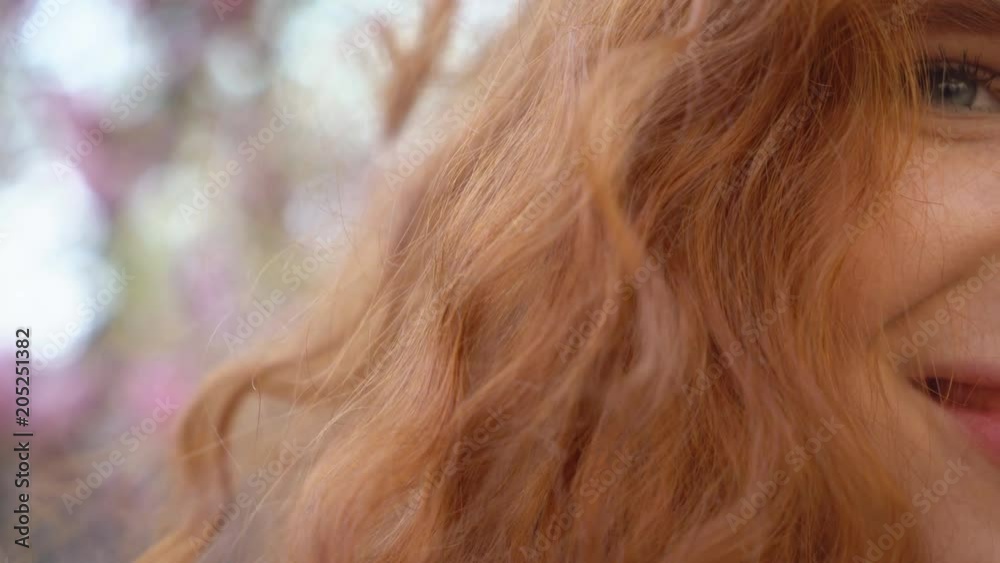 female portrait close-up. An amusing girl with natural red hair and blue eyes. in the background a blooming pink magnolia garden. spring freshness of the garden 4K female portrait close-up. An amusing girl with natural red hair and blue eyes. in the background a blooming pink magnolia garden. spring freshness of the garden 4K