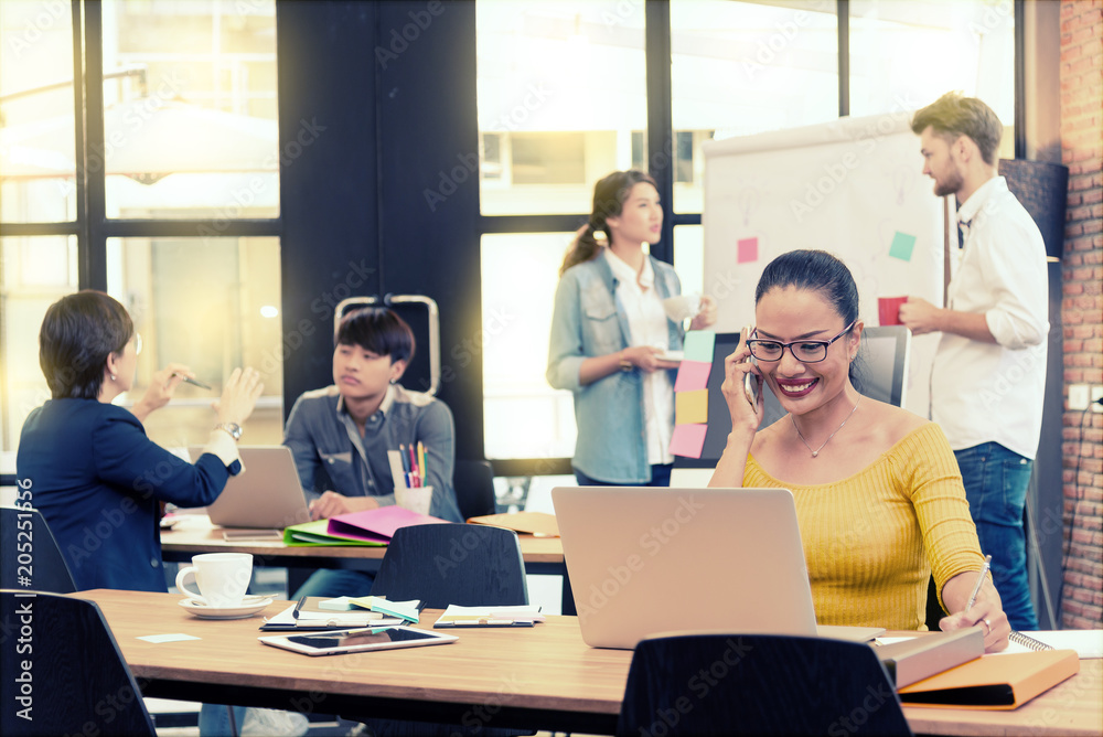 © livertoon - Asian charming beautiful business woman using smart phone for working in modern office and blurred multi ethnic business person group in casual suit in background. Project and Business concept.