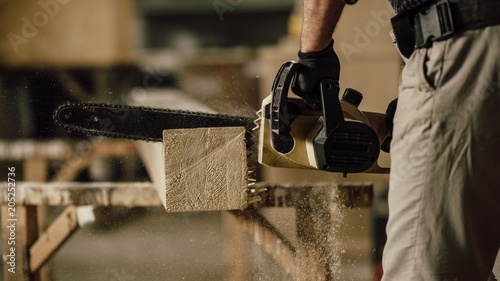 carpenter in the workshop saw a piece of wood with an electric chainsaw