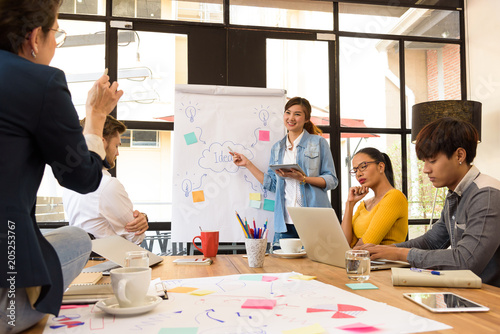 Asian young man business officer explaining internal meeting to his project team in modern office. They are the multi ethnic business person group in casual suit. Project and Business concept.