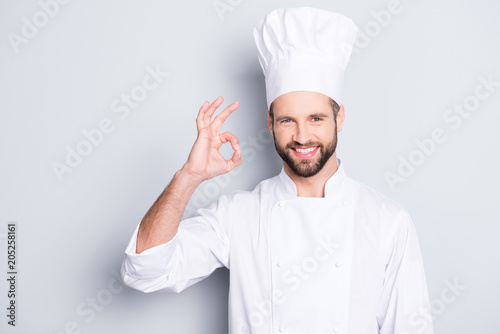 Portrait of cheerful joyful chef cook in beret and white outfit with stubble looking at camera showing ok sign, approve, advice menu isolated on grey background photo