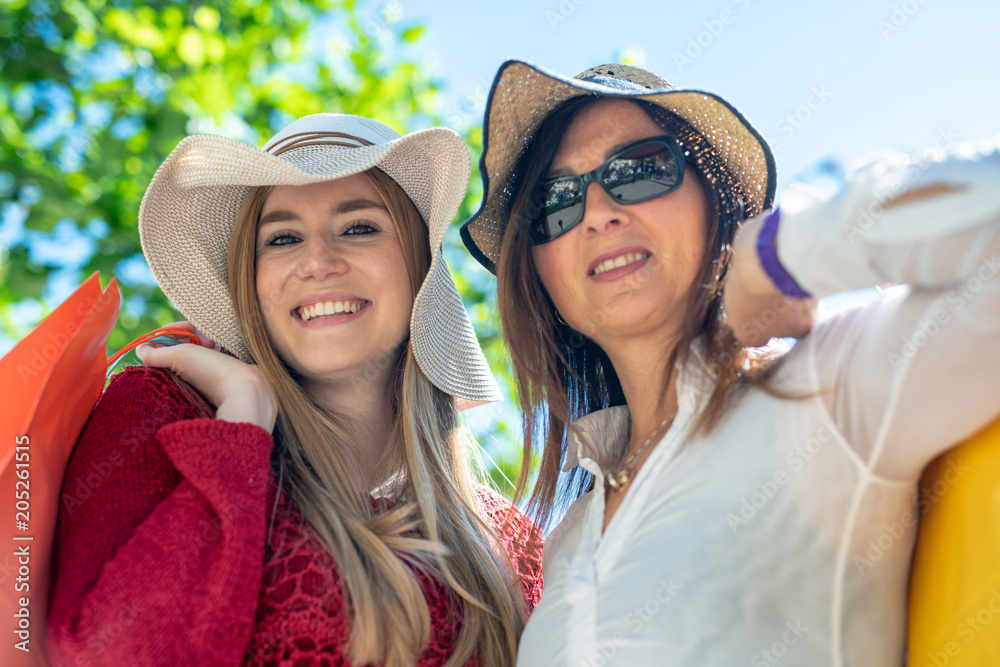 Two female tourists with straw hats enjoying outdoor city life with colourful gift bags