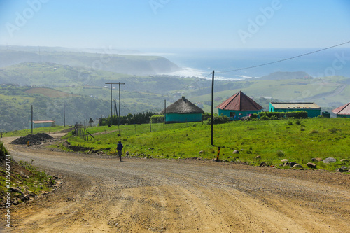 Two rondawels, traditional thatched-roofed huts on the side of a dirt road near Coffee Bay on the Wild Coast in Eastern Cape, South Africa, with a view over the Indian Ocean photo