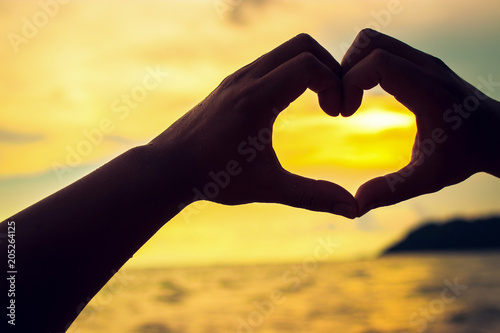 Beautiful silhouette of hand shape of love heart with sunset and beach background.