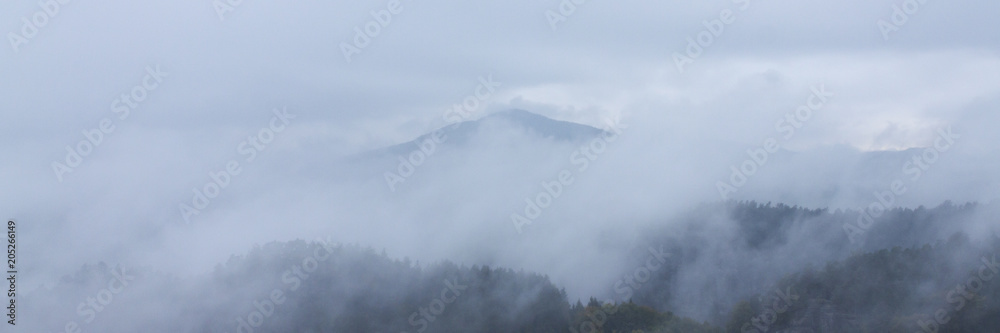 Panoramic view on peaks of mountains surrounded by clouds and fog
