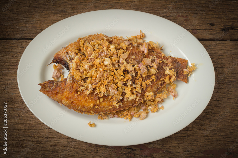 asia-asian food. thai food. fried nile tilapia river fish with garlic. on dish ceramic. on old wood background asia-asian food. thai food. fried nile tilapia river fish with garlic. on dish ceramic. on old wood background