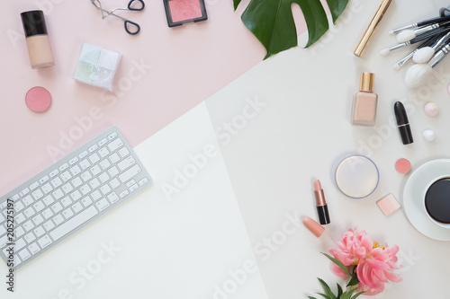 Top view of woman beauty blogger working desk with computer keyboard and laptop, notebook, decorative cosmetic, flowers and palm leaves, envelope on pink and white pastel table. Flat lay background.