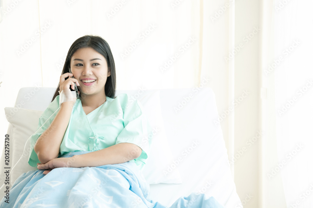 Patient talking on mobile phone in bed. Young attractive chinese woman in hospital bed. Connected world and mobile office concept. Patient talking on mobile phone in bed. Young attractive chinese woman in hospital bed. Connected world and mobile office concept.