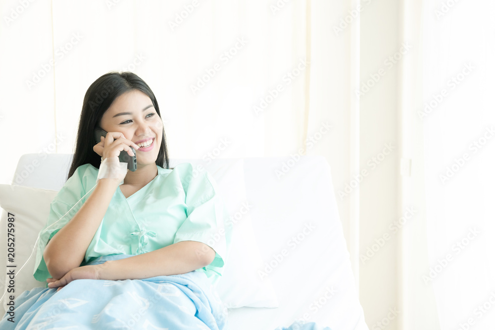 Patient talking on mobile phone in bed. Young attractive chinese woman in hospital bed. Connected world and mobile office concept. Patient talking on mobile phone in bed. Young attractive chinese woman in hospital bed. Connected world and mobile office concept.