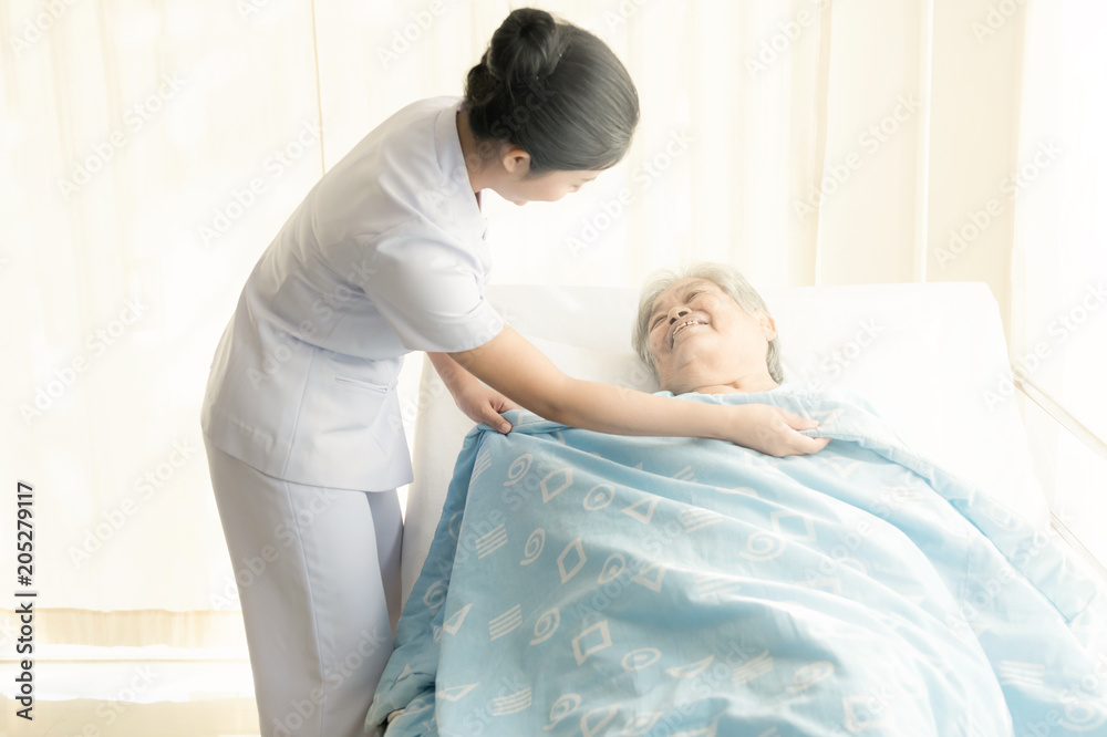 Obraz premium Nurse with patient. Routine health check and putting elderly patient to bed. Female nurse with senior chinese woman.