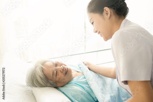 Nurse with patient. Routine health check and putting elderly patient to bed. Female nurse with senior chinese woman.