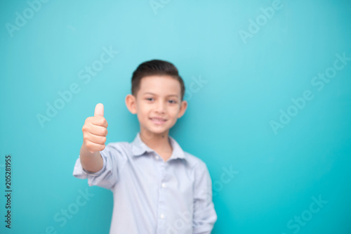 Young boy isolated in blue. Handsome early teenage boy portrait. Happy smile thump up pose.