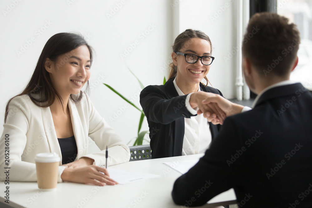 Back view of businessman shaking hand of smiling female colleague greeting her at board meeting, making good first impression. Concept of partnership, cooperation, diversity. Women in business Back view of businessman shaking hand of smiling female colleague greeting her at board meeting, making good first impression. Concept of partnership, cooperation, diversity. Women in business