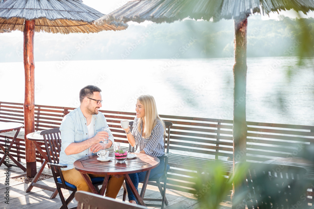 Happy young couple drinking coffee and talking while relaxing in a riverside cafe. Romantic vacation moments