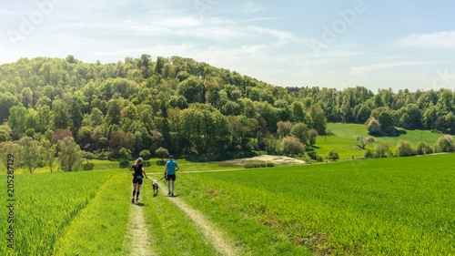 Mann und Frau laufen mit einem Hund einen Feldweg bei wunderschönem Wetter entlang photo