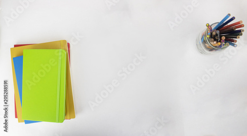 An artistic desk on an isolated white background with colored pencils and notebooks 