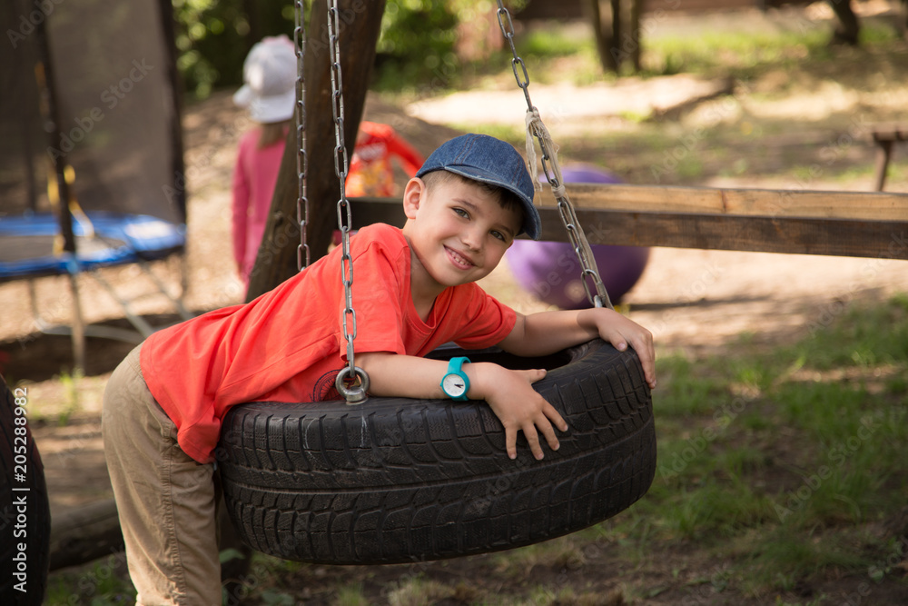A smiling kindergarten boy on a tire swing