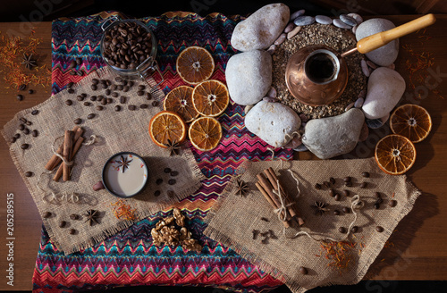 Сoffee table with the cezva on sand and patterned tablecloth in Oriental style. Scattered coffee beans and spices. Top view