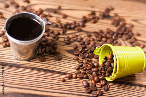 Full zinked bucket of black coffee near roasted beans poured out of green metal bucket with handle on old worn wooden table photo